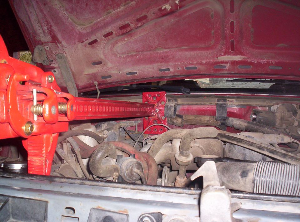 Red hi-lift jack positioned over engine components in a red vehicle's engine bay