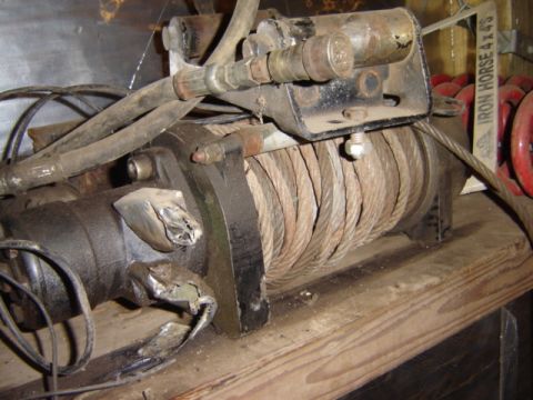 1992 Ford Bronco - A hydraulic winch with coiled steel cable and hydraulic lines is mounted on a wooden surface.
