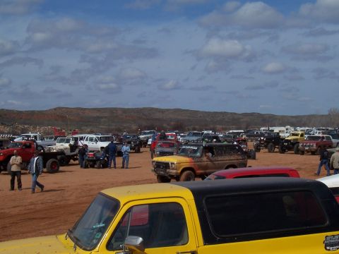 2004 Aston Martin Virage - A large gathering of off-road vehicles are parked in a dusty, muddy field under a partly cloudy sky.