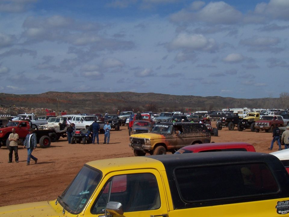 Muddy off-road vehicles parked in a dirt field under a cloudy sky