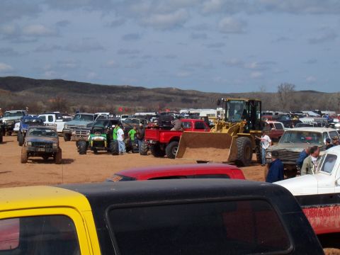 2004 Aston Martin Virage - A large gathering of off-road vehicles and heavy equipment is seen on a dusty lot with hills in the background.