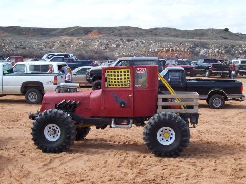 2004 Aston Martin Virage - Custom off-road vehicle with large tires parked in a sandy area with other vehicles.