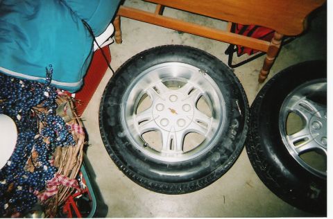 2000 Ford Crown Victoria - A close-up view of two tires and rims, one with a silver alloy wheel, resting on a concrete floor.