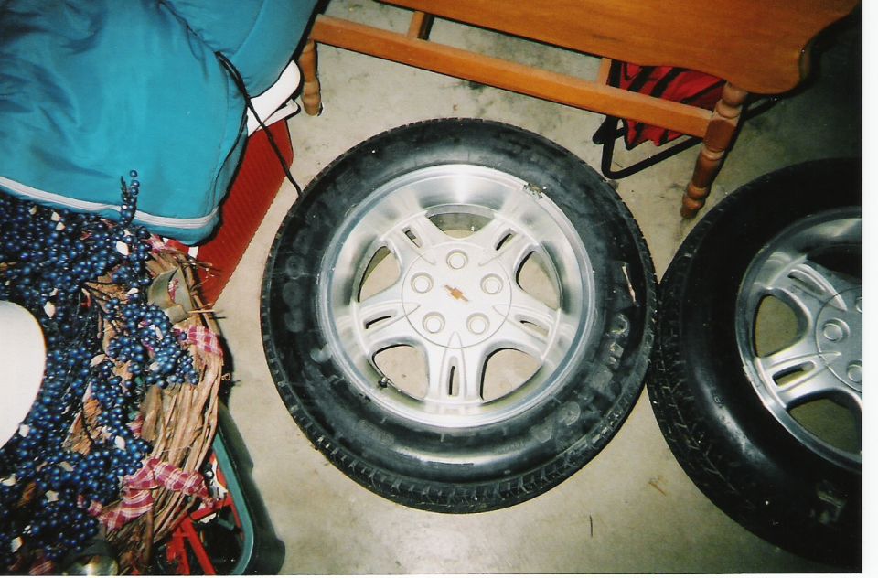 Two car tires and rims are on the floor next to some blue fabric and a wooden table leg