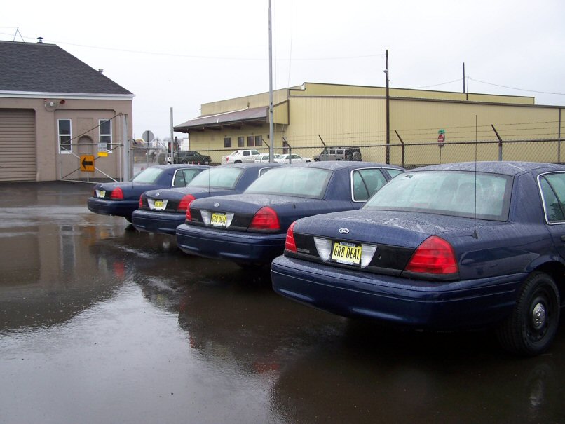 Four dark blue 2001 Ford Crown Victoria police cars parked in a wet lot