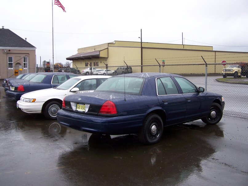 Dark blue 2001 Ford Crown Victoria police car parked in lot with other vehicles, license plate reads GR8 DEAL