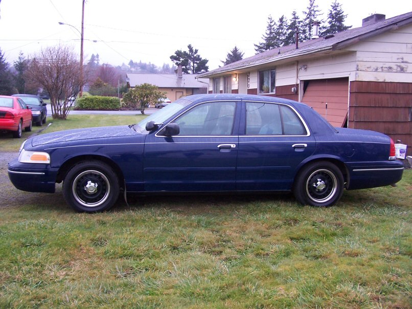 1998 Ford Crown Victoria sedan, dark blue, parked on grass in front of a house