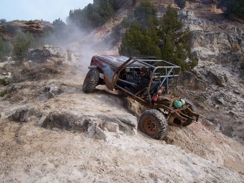 Off-road buggy with roll cage climbing a rocky incline, kicking up dust