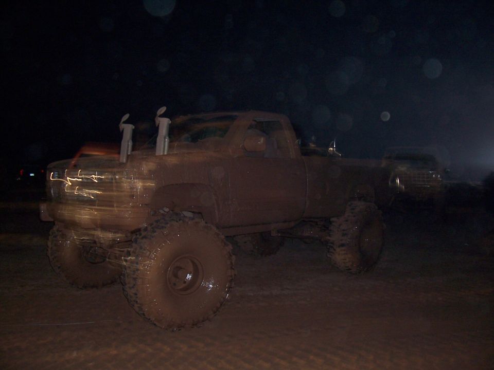 Mud-covered pickup truck with dual exhaust stacks, seen at night