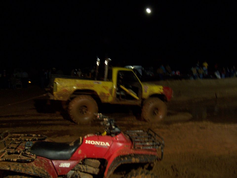 Yellow pickup truck with large tires and exhaust stacks in a mud bog at night