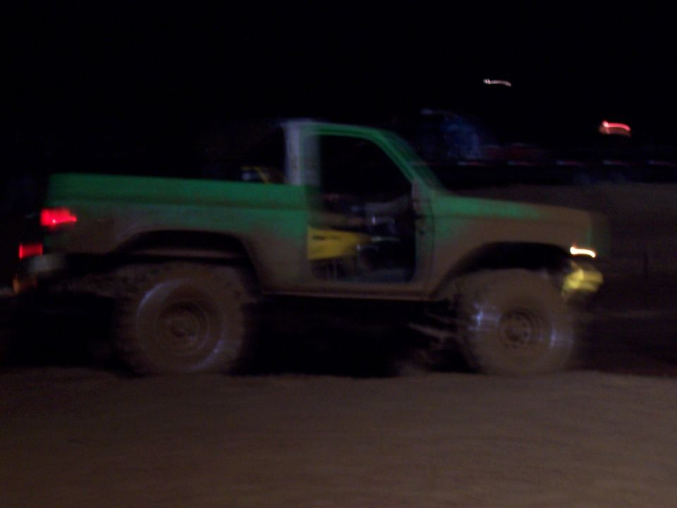 Mud-covered green pickup truck with open driver's door, seen from the side at night