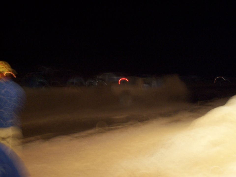 Blurry red and yellow lights streak across a dark, sandy landscape at night