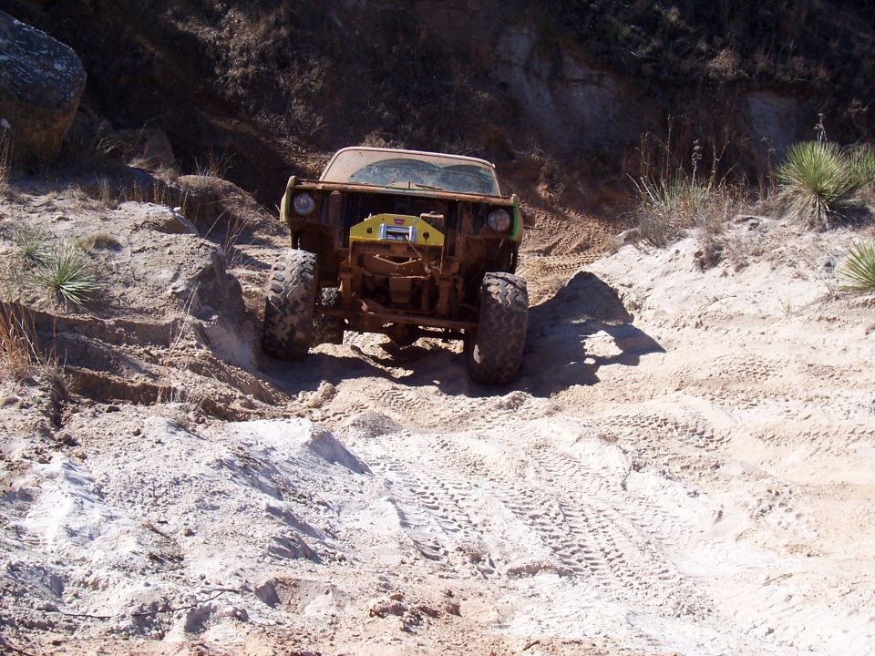 Muddy off-road vehicle with a winch on the front, driving through sandy terrain