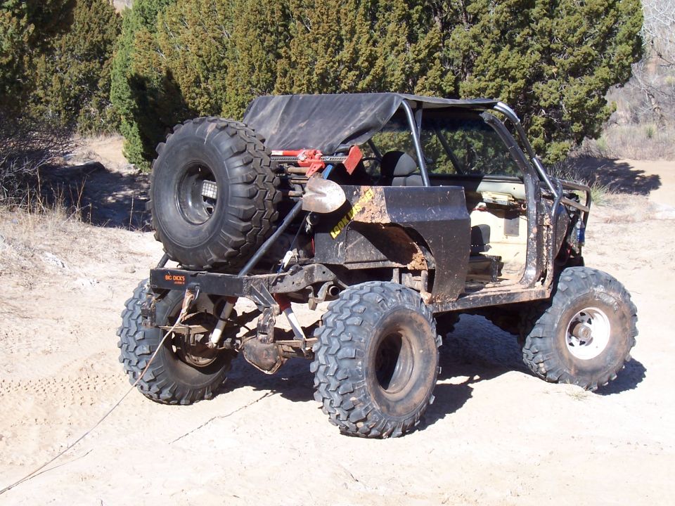 Off-road buggy rear view with large tires, spare on back, and shovel mounted