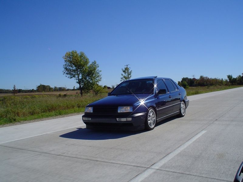 dark blue sedan driving on a highway, sun reflecting off the paint