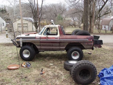 1979 Ford Bronco - This modified Ford Bronco sits in a grassy yard with spare tires and tools nearby.