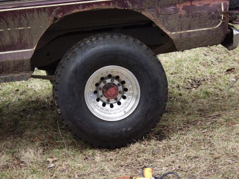 1979 Ford Bronco - Close-up of the rear wheel and fender of a muddy SUV, showing off its large tires and aftermarket rims.
