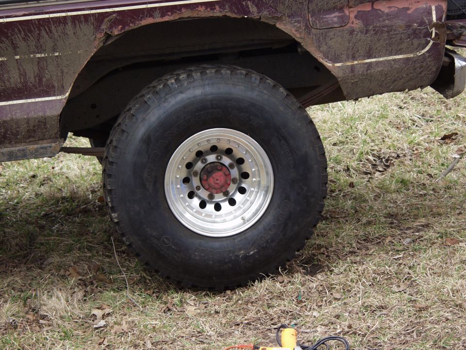 Oversized Goodyear mud tire on polished wheel under a rusted maroon truck fender