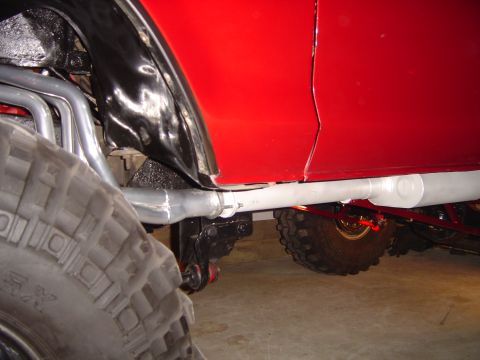 1978 Ford Bronco - Close-up view of a red vehicle's side, highlighting its large tires, custom exhaust, and suspension.