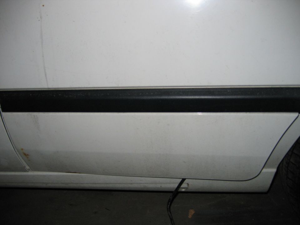 Close-up of white car door with black trim and rust spot