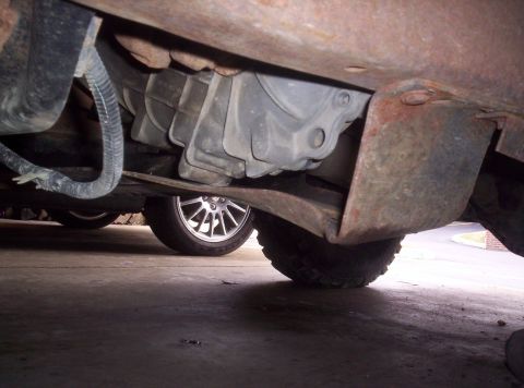 1989 Ford Bronco - A low-angle shot reveals the undercarriage of a vehicle, including drivetrain components and wheels, with a watermark at the bottom right.