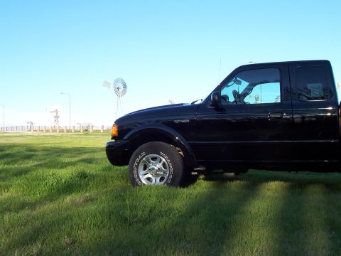 2003 Ford Ranger - Side view of a black 2003 Ford Ranger pickup truck parked in a grassy field with windmills in the background.