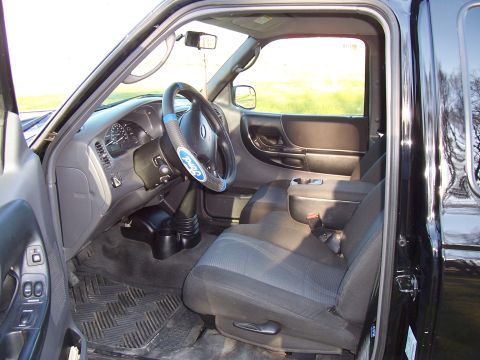 2003 Ford Ranger - The interior of a black 2003 Ford Ranger pickup truck, fabric seats and a Ford-branded steering wheel cover.