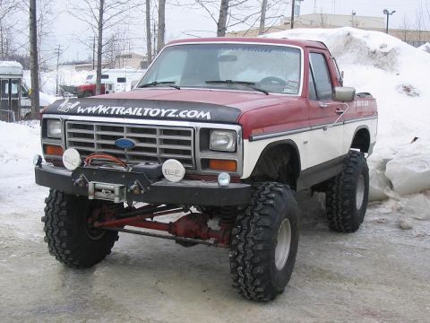 1985 Ford Bronco - This lifted pickup truck features aggressive off-road tires, a front winch, and a two-tone red and white paint scheme.