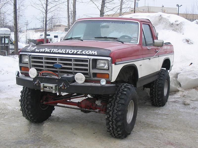 Lifted red and white Ford Bronco on big mud tires with winch bumper in snow