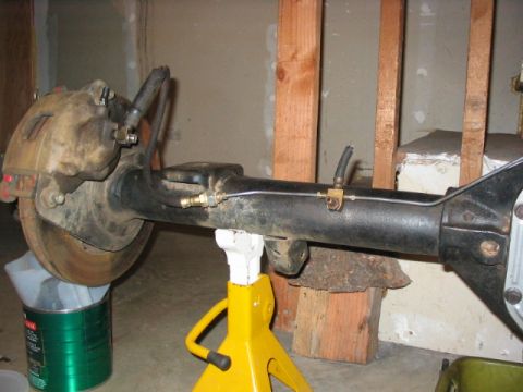 1995 Ford Bronco - Rear axle assembly with brake caliper and brake lines, supported by a jack stand, likely undergoing modification or repair.