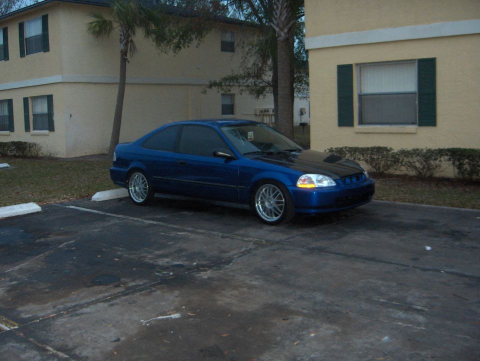 Blue coupe with a black hood parked in a lot, 3/4 front view