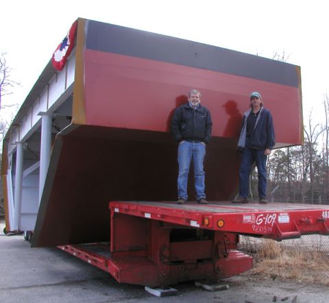1988 Ford Bronco - A large, unusually shaped cargo is being transported on a flatbed trailer, with two individuals standing nearby.