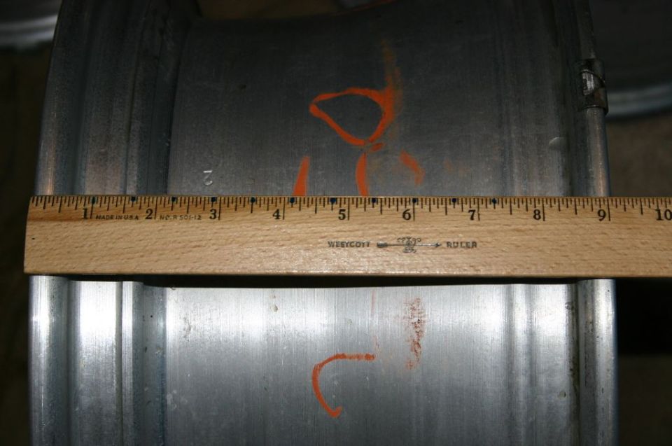 Close-up of a metal wheel rim with orange spray paint marks and a wooden ruler measuring its width