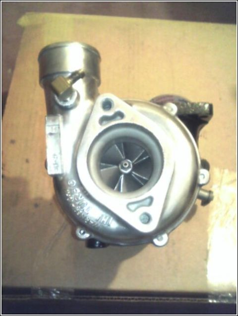 1989 Mazda MX-6 - A turbocharger sits on a surface, showing its internal components and external connections.