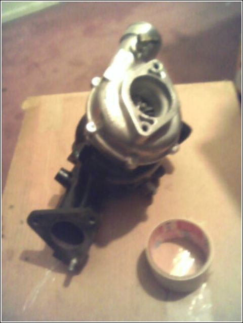1989 Mazda MX-6 - Turbocharger shown on a flat surface, with a small container of liquid nearby.