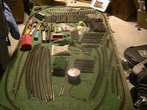 1981 Chevrolet C/K Pickup - A collection of model train tracks, buildings, and vehicles are spread out on a green mat, ready for assembly.