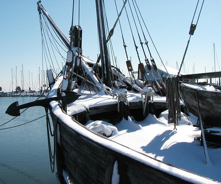 Snow-covered wooden sailing ship at a marina dock under a clear blue sky