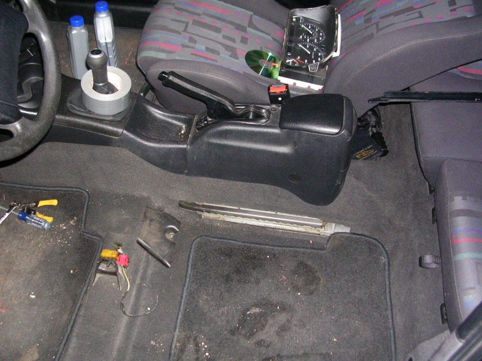 Car interior teardown with removed gauge cluster on seat and tools on the carpet