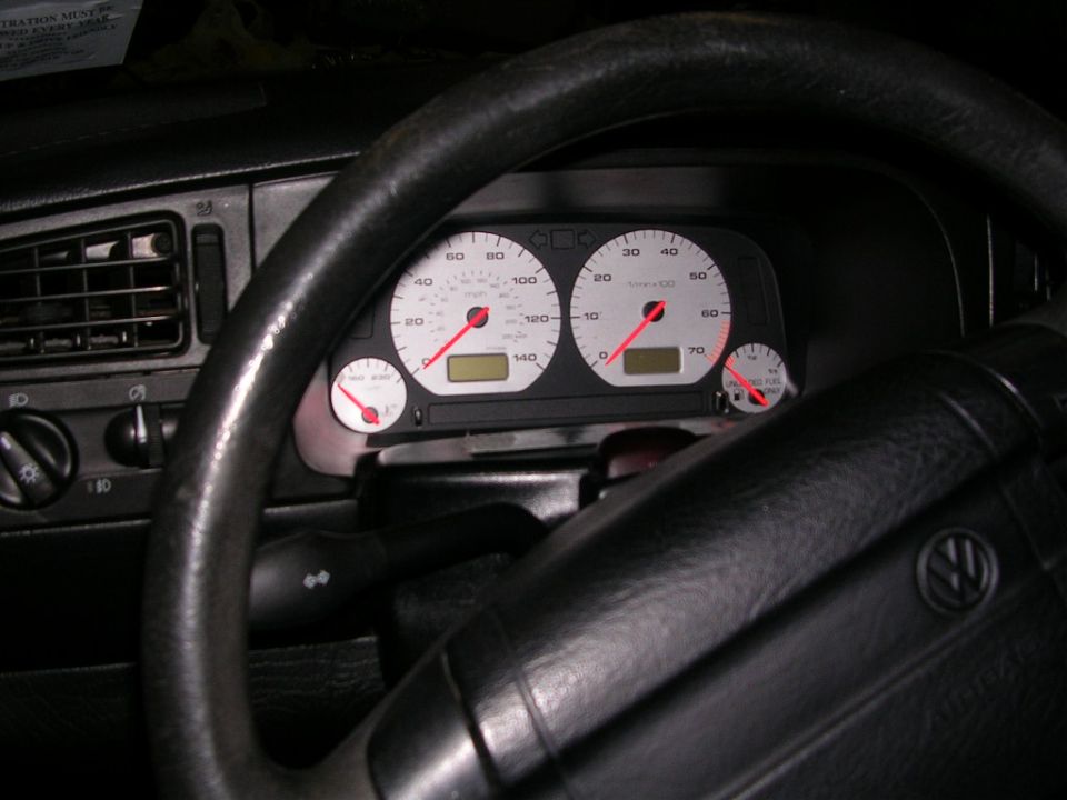 VW instrument cluster with white gauge faces and red needles behind a black steering wheel
