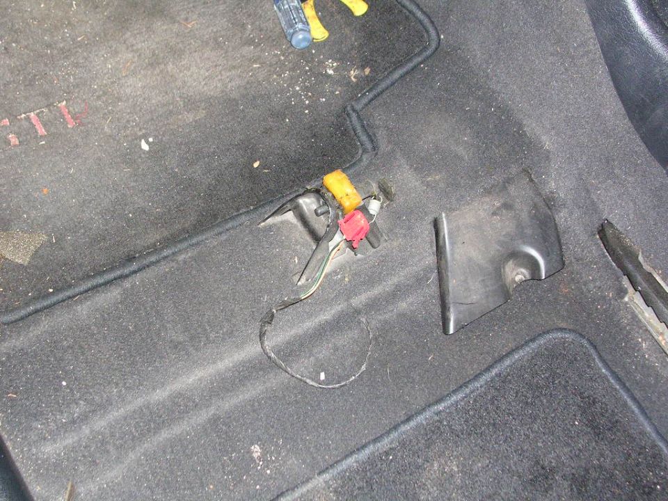 Car floor carpet with exposed yellow and red airbag connectors and removed trim cover