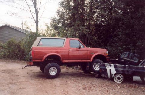 1995 Ford Bronco - A red 1995 Ford Bronco is loaded onto a trailer alongside a black car.