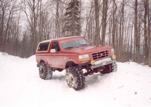 1995 Ford Bronco - A red 1995 Ford Bronco navigates a snowy terrain with its large tires.