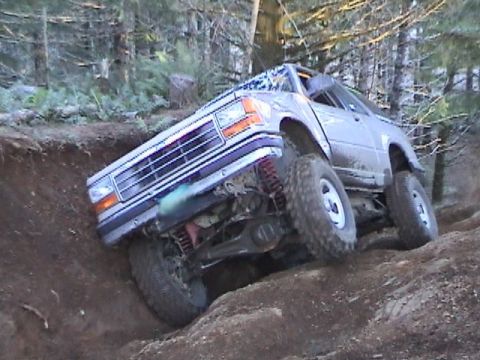 1994 Ford Explorer - This modified SUV is navigating a steep, muddy trail with its wheels at extreme angles.