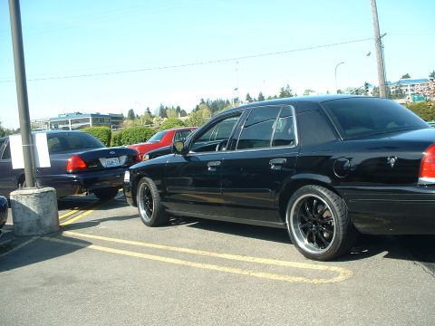 1998 Ford Crown Victoria - A black 1998 Ford Crown Victoria sedan is parked next to another vehicle, its custom wheels.