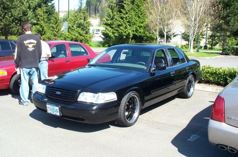 1998 Ford Crown Victoria - A black 1998 Ford Crown Victoria is parked outdoors with other vehicles nearby.