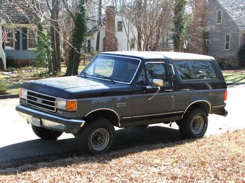 1996 Ford Bronco - This Ford Bronco SUV is parked on a street with houses and trees in the background.