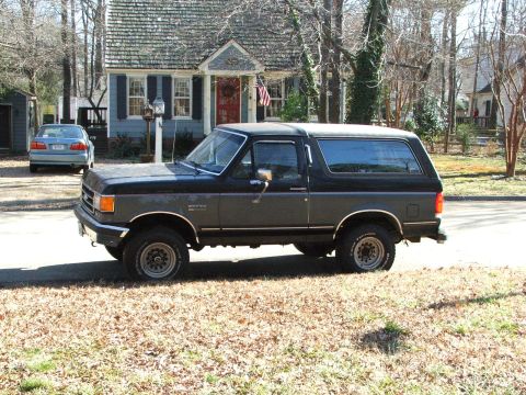 1996 Ford Bronco - A two-tone Ford Bronco is parked in front of a house with a blue sedan in the background.