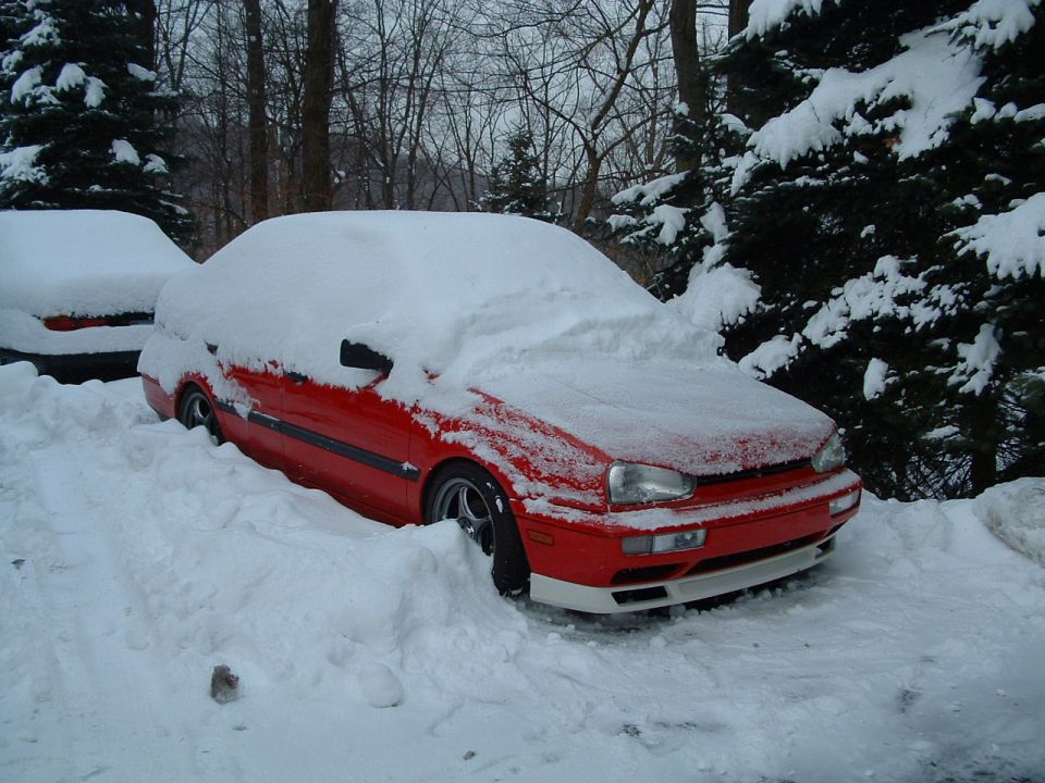 red sedan buried in snow, another car visible behind it