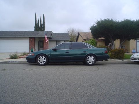1993 Ford Taurus - Side view of a green sedan parked on a residential street.