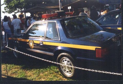 1991 Ford Mustang - A 1991 Ford Mustang SSP police car is parked outdoors with a crowd in the background.